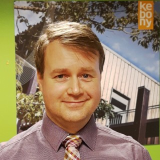 Nærbilde av en mann med et trehus i bakgrunnen