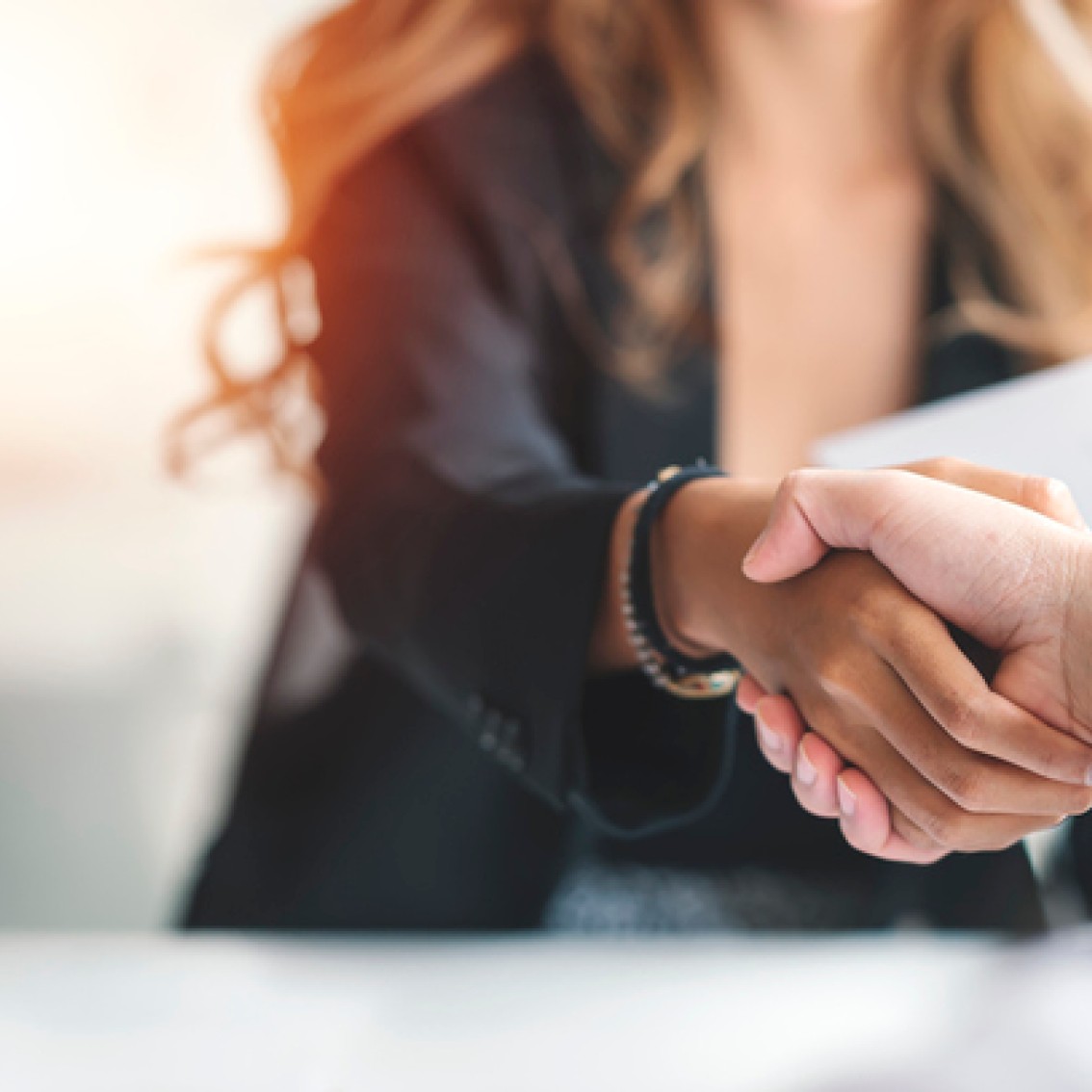 To personer gir hverandre et håndtrykk over bordet