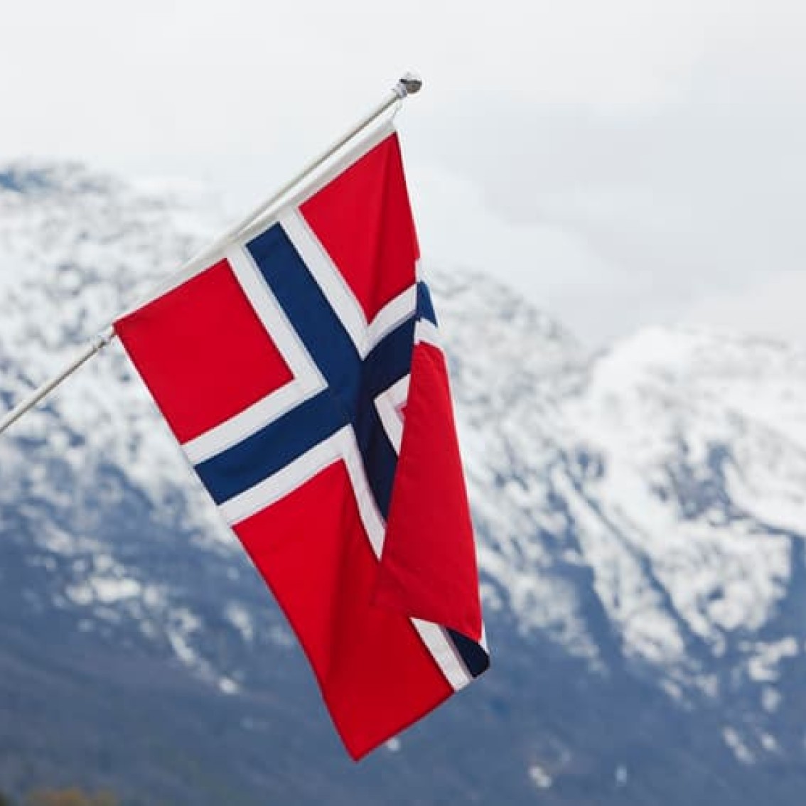 Norsk flagg i rødt, hvitt og blått med et snødekt fjell i bakgrunnen.